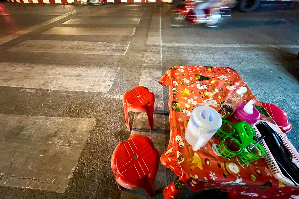 Une table et des tabourets en plastique posés sur la rue au bord d’un passage piéton.