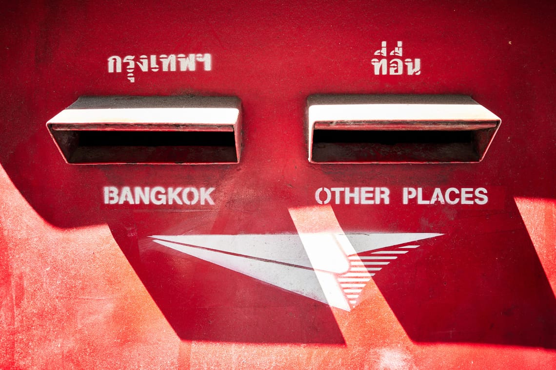 Gros plan d’une boîte aux lettres rouge avec deux fentes: Bangkok et Other Places.