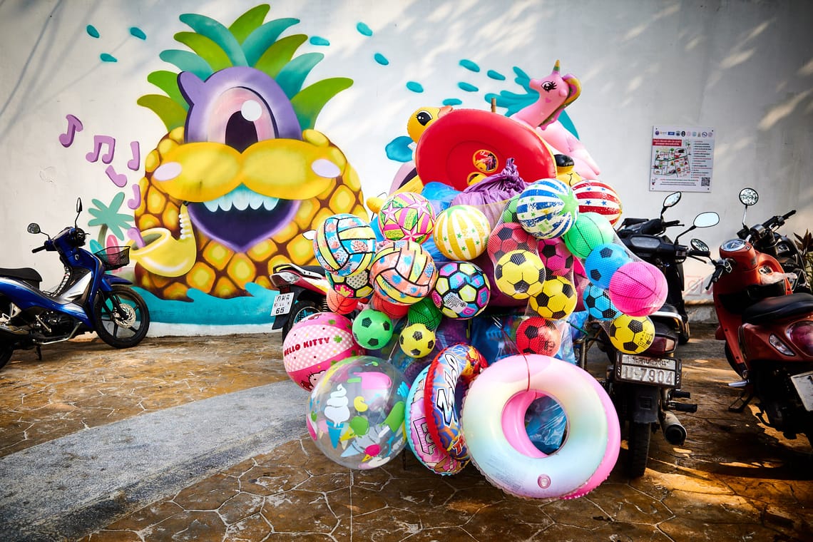 Devant un mur peint, moto d’un marchand disparaissant sous des ballons et bouées multicolores.