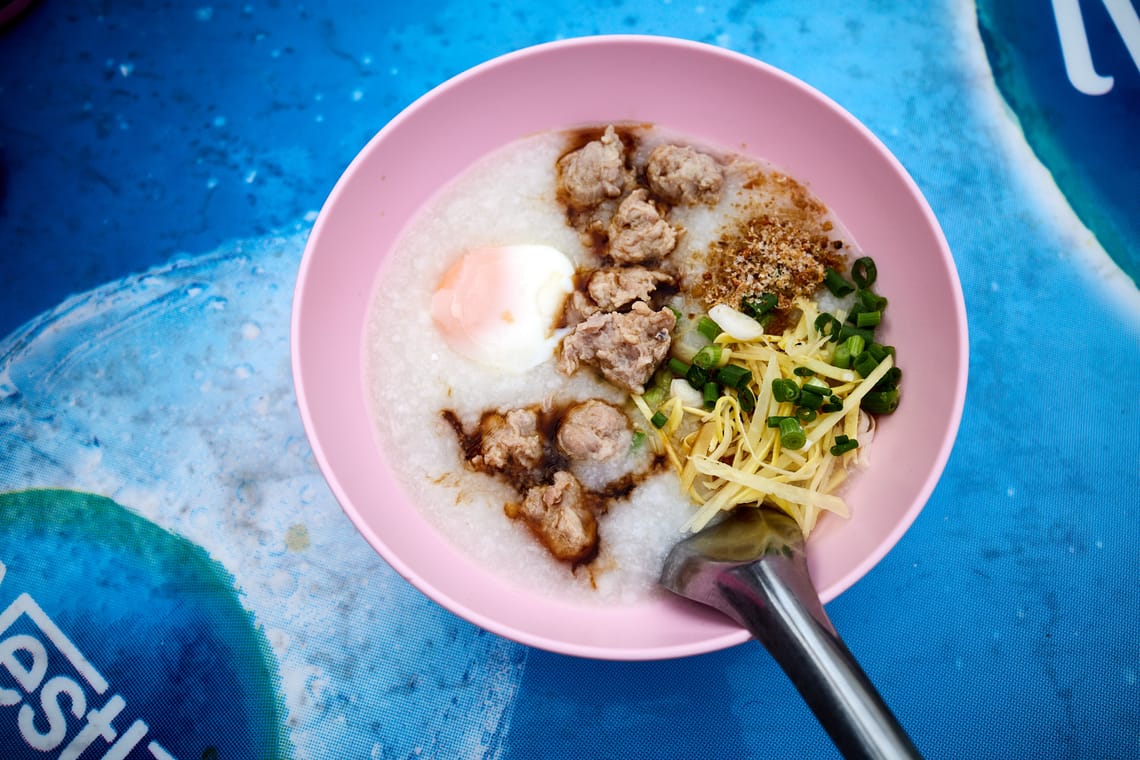 Soupe de riz thaï (jok) dans un bol rose sur une table bleue.