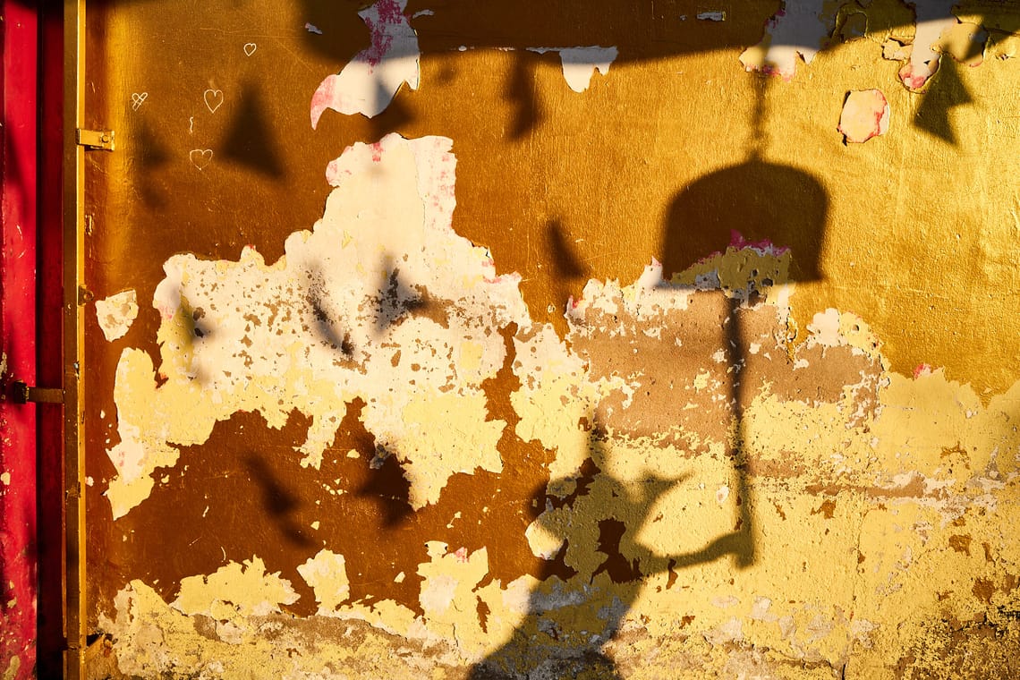 Dans une lumière chaude, sur un mur décrépi aux reflets dorés, l’ombre d’un enfant qui fait sonner la cloche du temple.